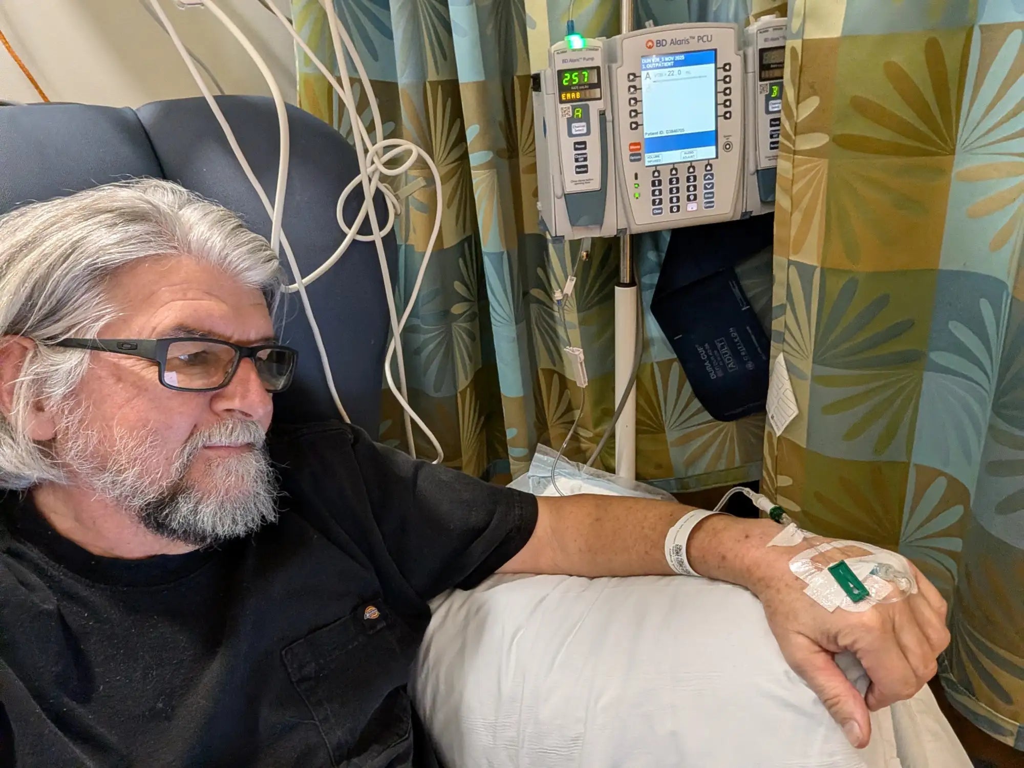 gallery position 1 showing man with gray hair and glasses receiving IV treatment in hospital Support Greg Profits Pay for Alzheimer’s Treatments