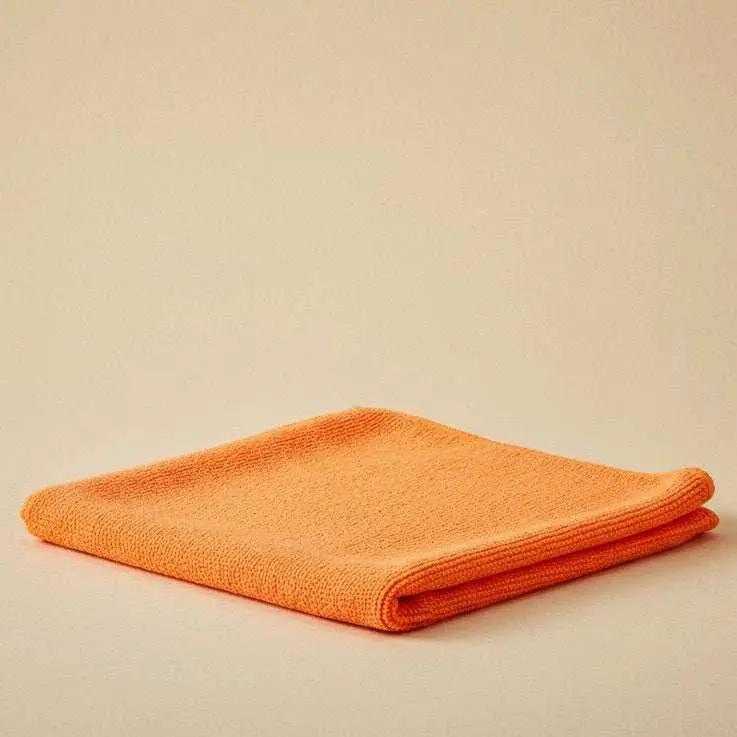 Folded orange microfiber cleaning cloth on a beige background