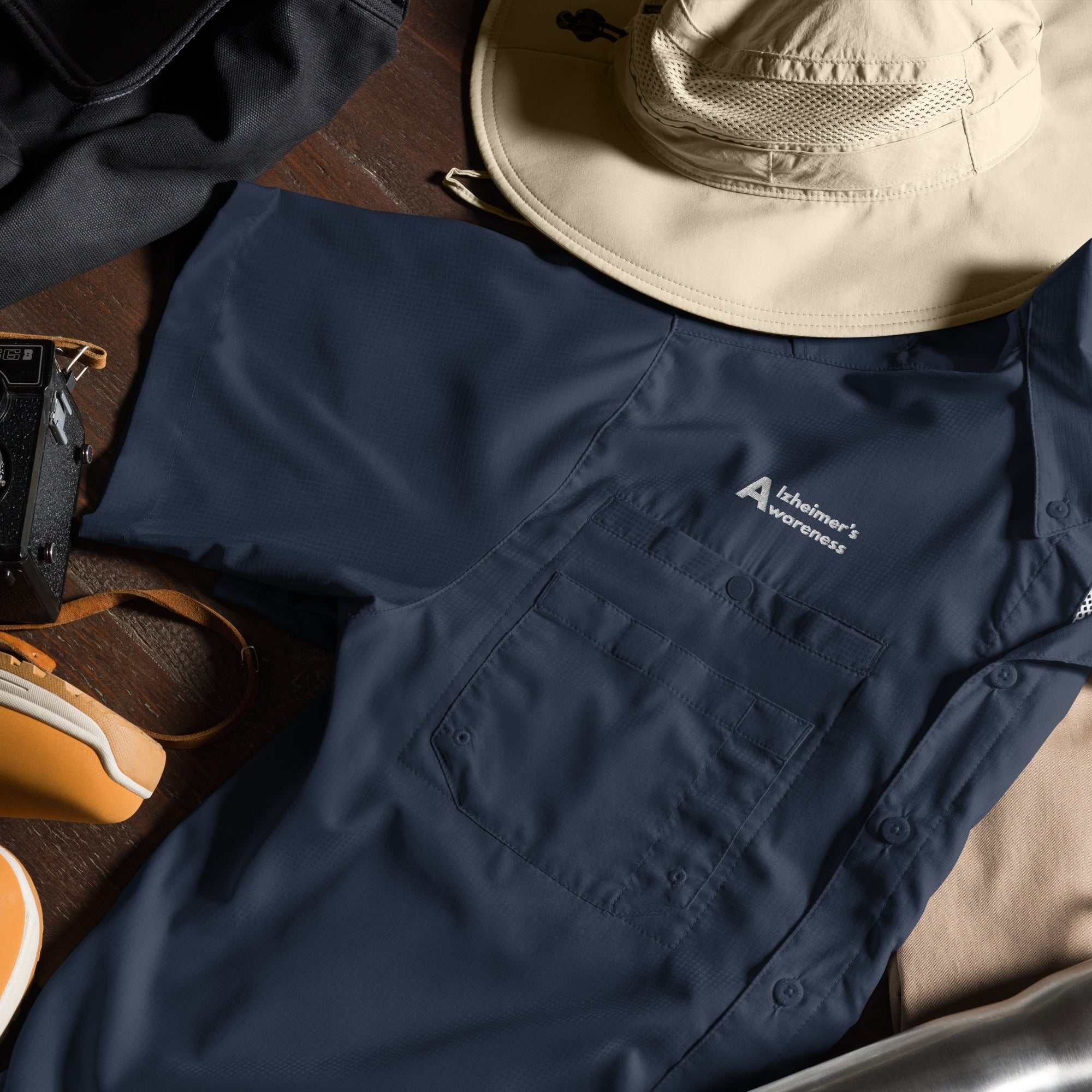 Mens Columbia Alzheimers Awareness short sleeve shirt with pocket and logo on wooden surface with hat and camera