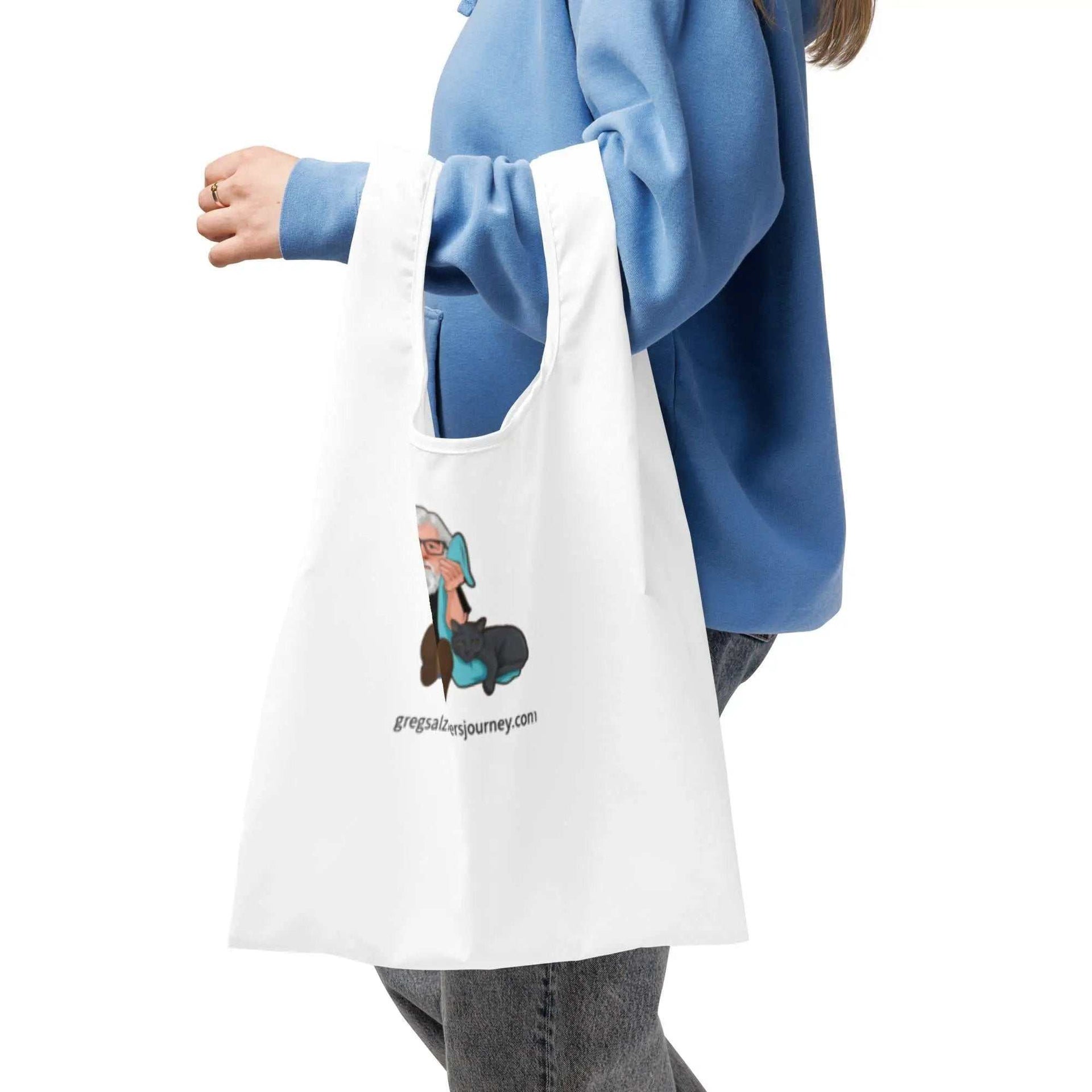 Person carrying a white The Cat Man signature shopping bag with a graphic of a man and cat